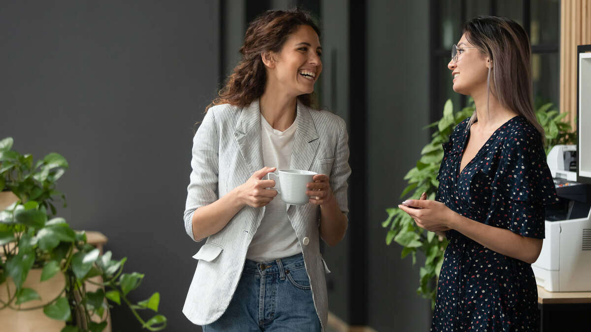 Woman CEO holds coffee and talks with employee in hallway