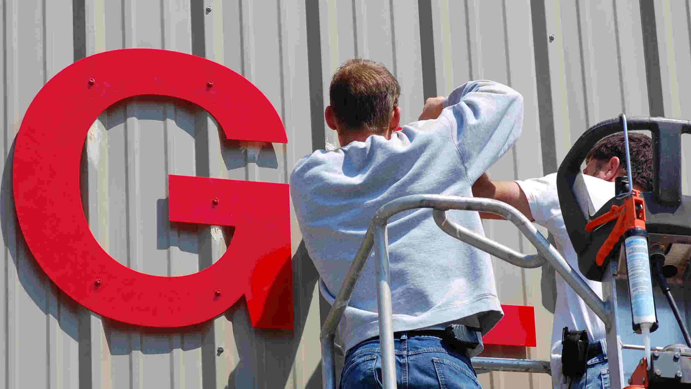 Two men on lift install large red letters on side of budiling