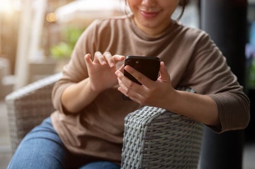 Woman on wicker chair checks email on phone.