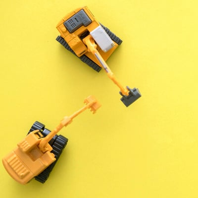 Two yellow toy construction trucks sit together on yellow background.